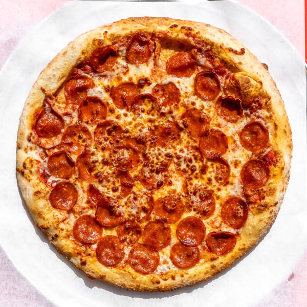 Round pepperoni pizza with melted cheese on white paper, on a metal tray, against a red background.