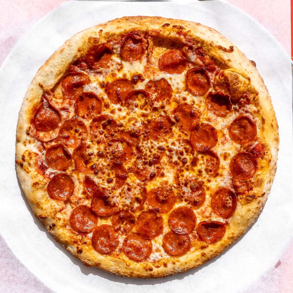 Round pepperoni pizza with melted cheese on white paper, on a metal tray, against a red background.