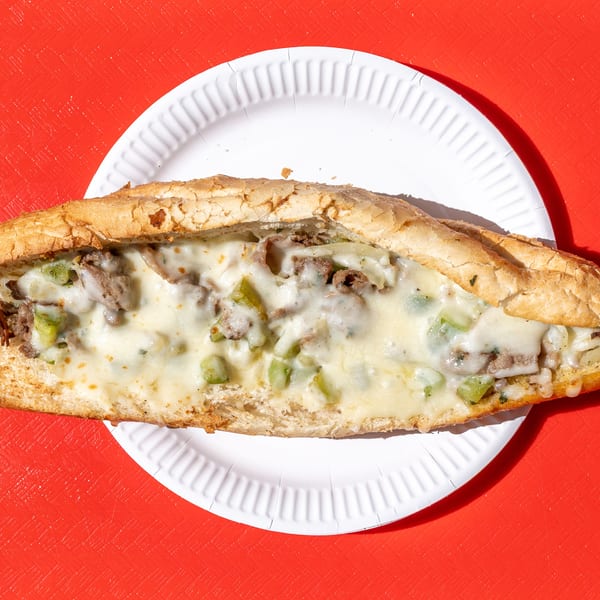 Cheesesteak sandwich with melted cheese, steak, and green peppers on a white paper plate.