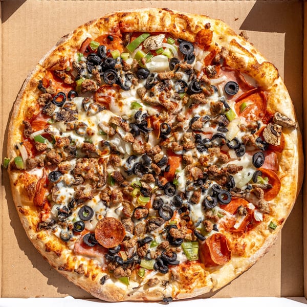 Overhead view of a loaded pizza with pepperoni, sausage, olives, peppers, and mushrooms in a box.