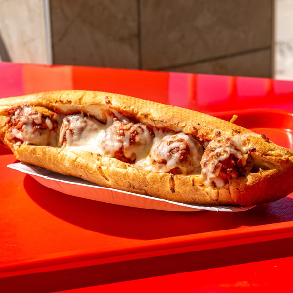 A long meatball sub with melted mozzarella and marinara sauce, served on a bright red tray.