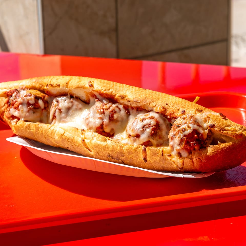 A long meatball sub with melted mozzarella and marinara sauce, served on a bright red tray.